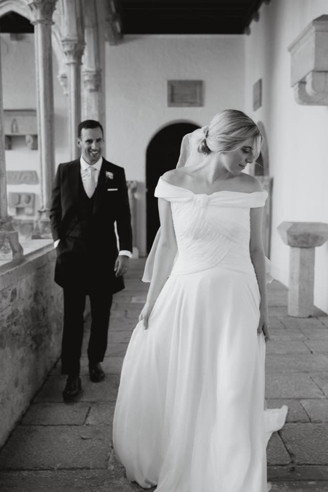 Los novios caminan por la galería de un claustro en blanco y negro