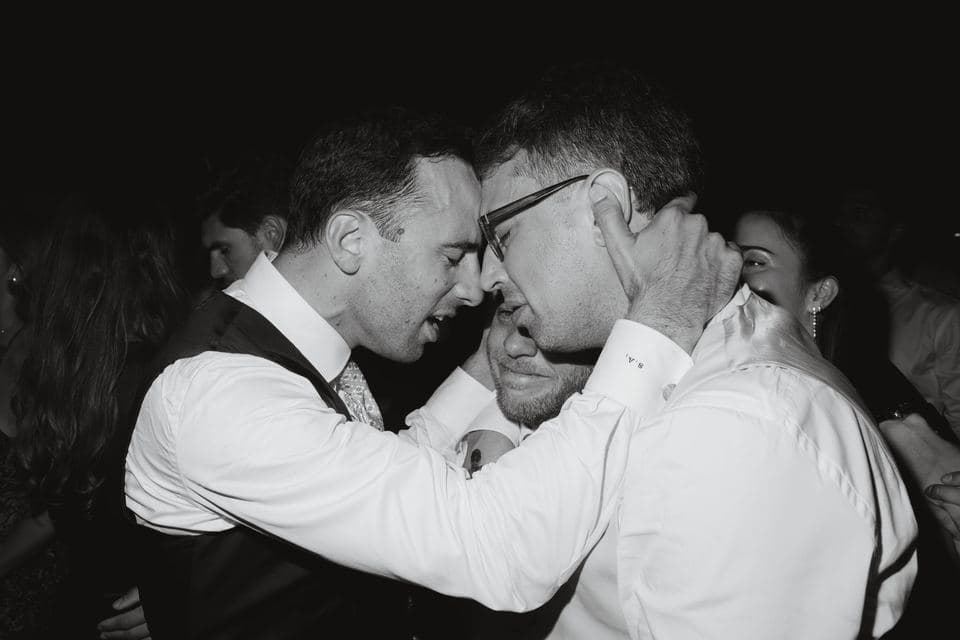 Dos invitados se abrazan emocionados en la pista de baile de una boda, en blanco y negro