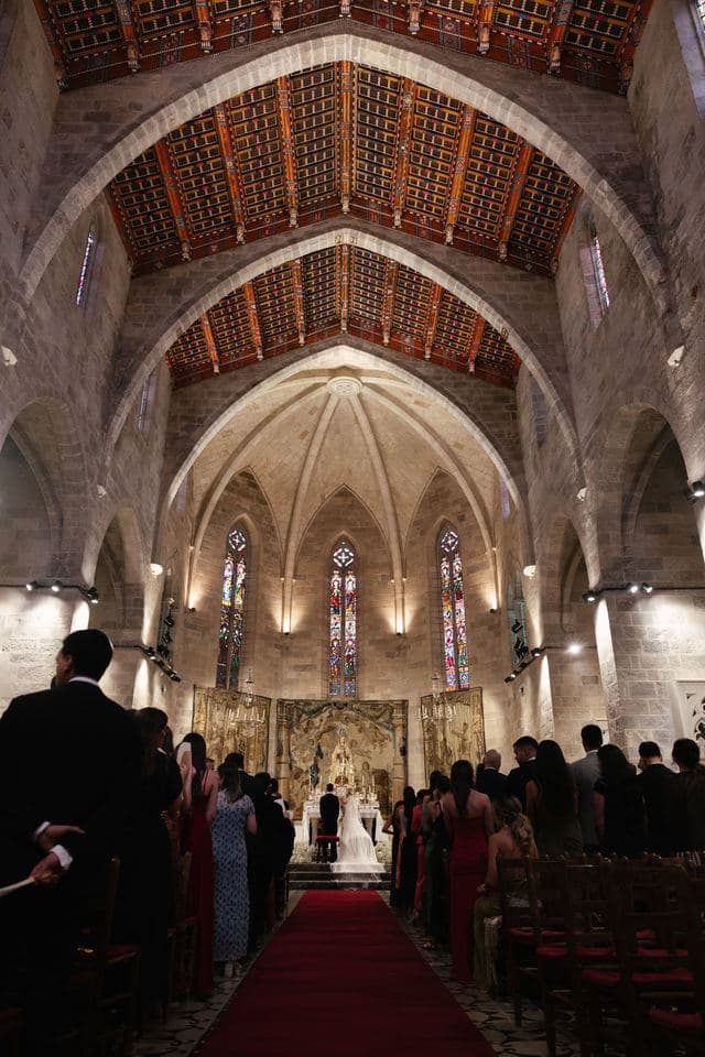 Ceremonia de boda en el interior de una iglesia gótica, con los invitados de pie a ambos lados de la alfombra roja