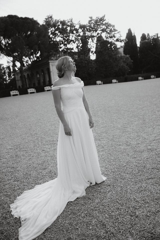 Retrato en blanco y negro de la novia de pie en el jardín de una finca, mirando hacia la luz